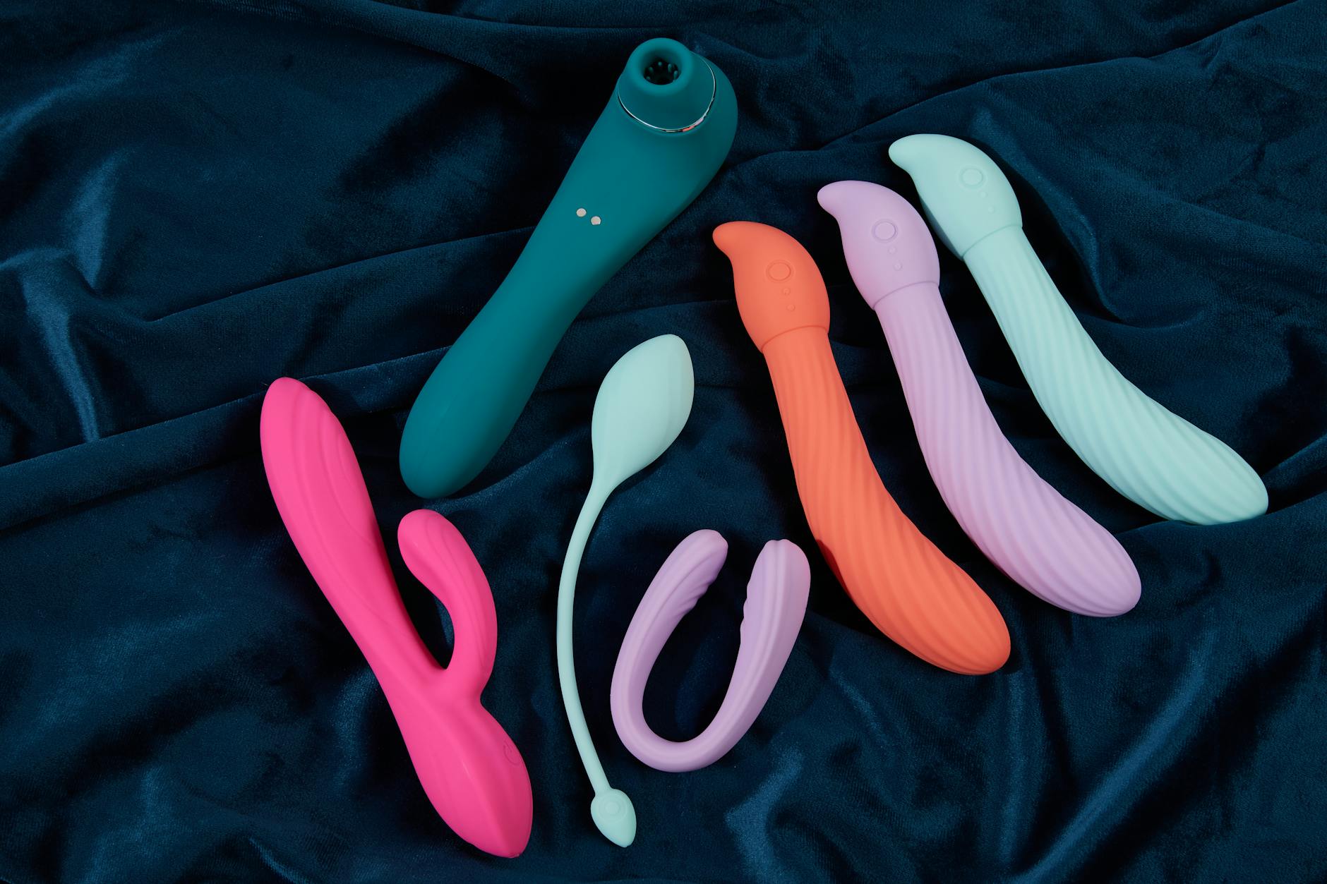 Hand reaching toward colorful clitoral vibrators arranged on table
