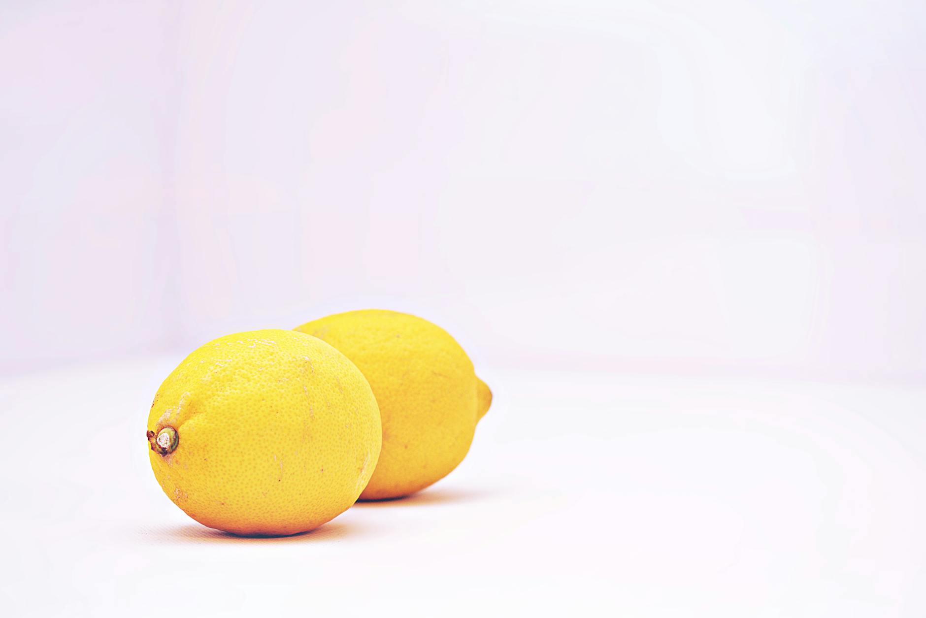Two fresh lemons on a minimalist white background, symbolizing refreshed sensation and vitality