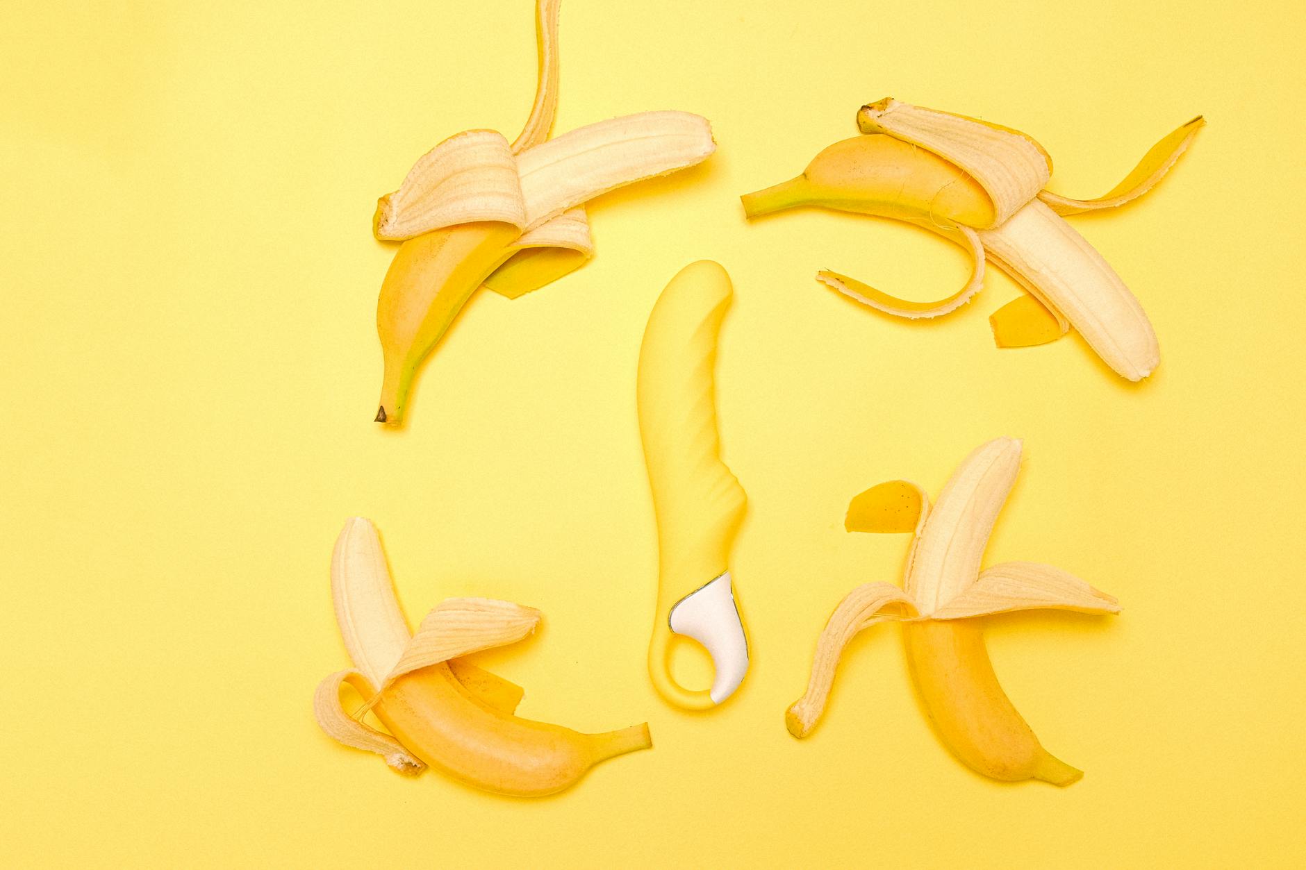 A yellow silicone lemon clitoral vibrator surrounded by fresh lemons on a bright yellow background.