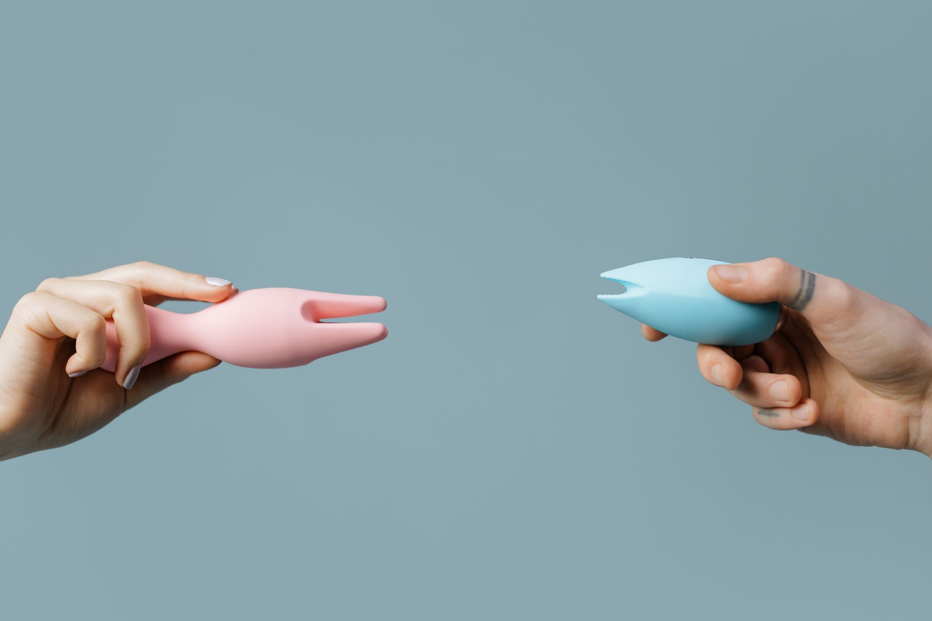 Close-up of hands holding colorful vibrators against a pastel background