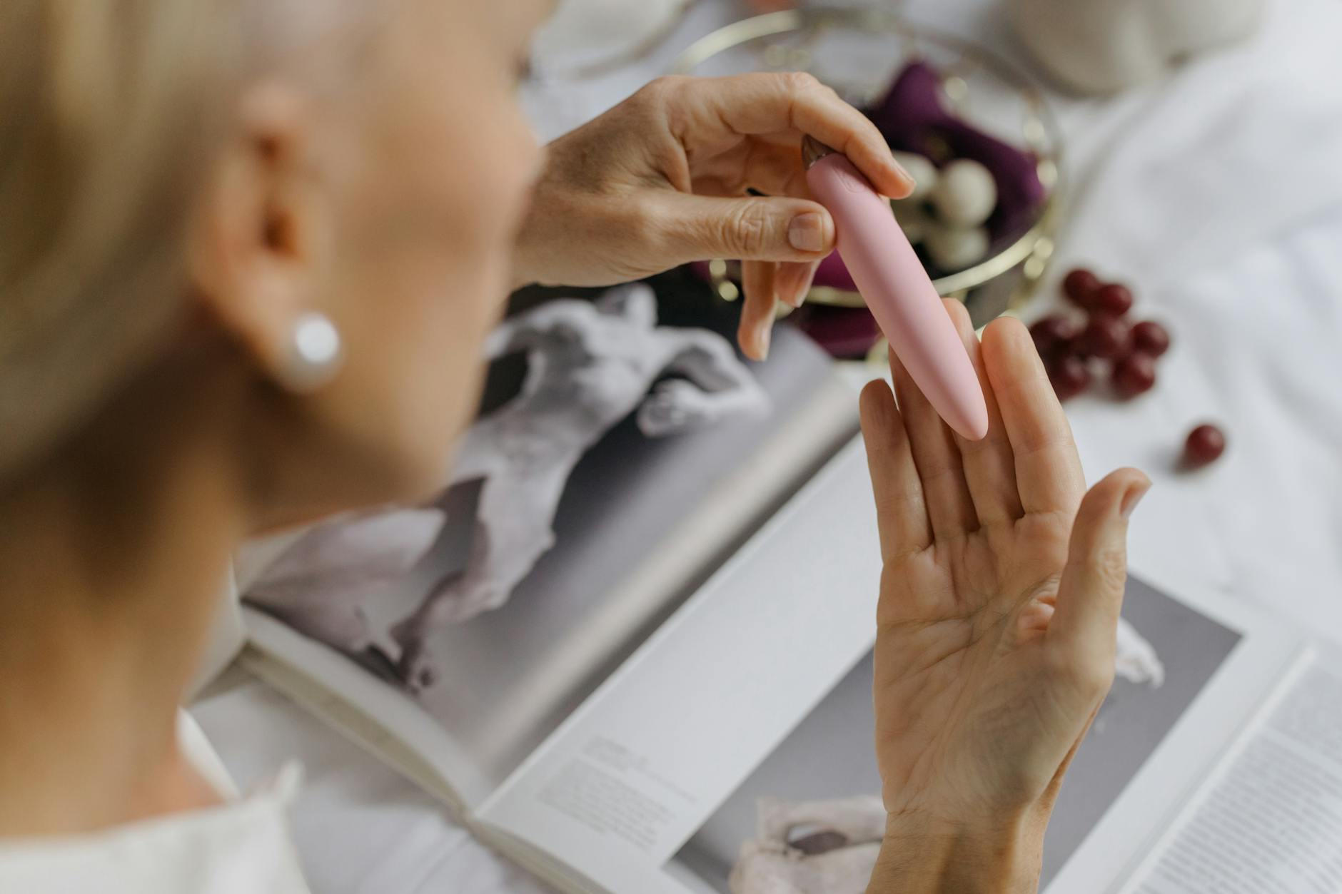 Close-up of a person holding a pink vibrator with personal care items in the background