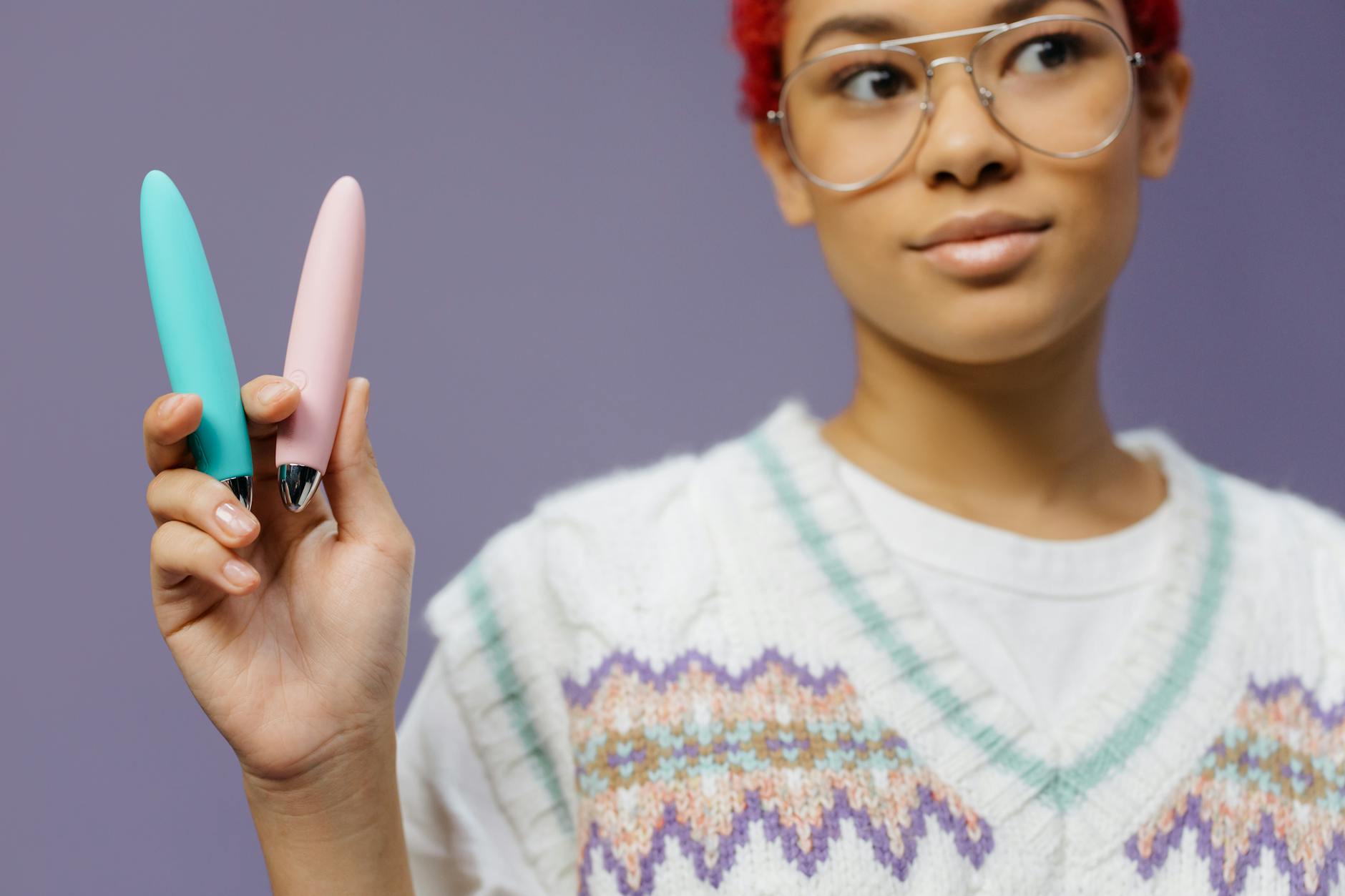 A woman holding colorful vibrators against a purple background, exploring pleasure options without penetration