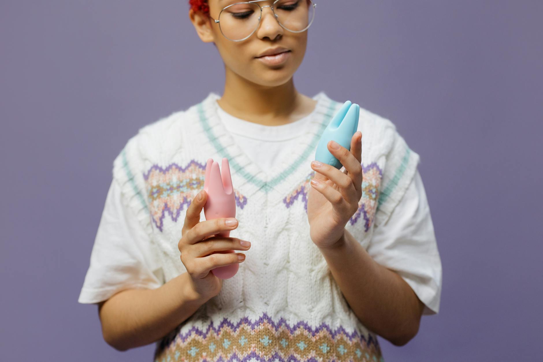 Woman with eyeglasses thoughtfully holding a blue vibrator, representing intentional self-discovery and pleasure reclamation.