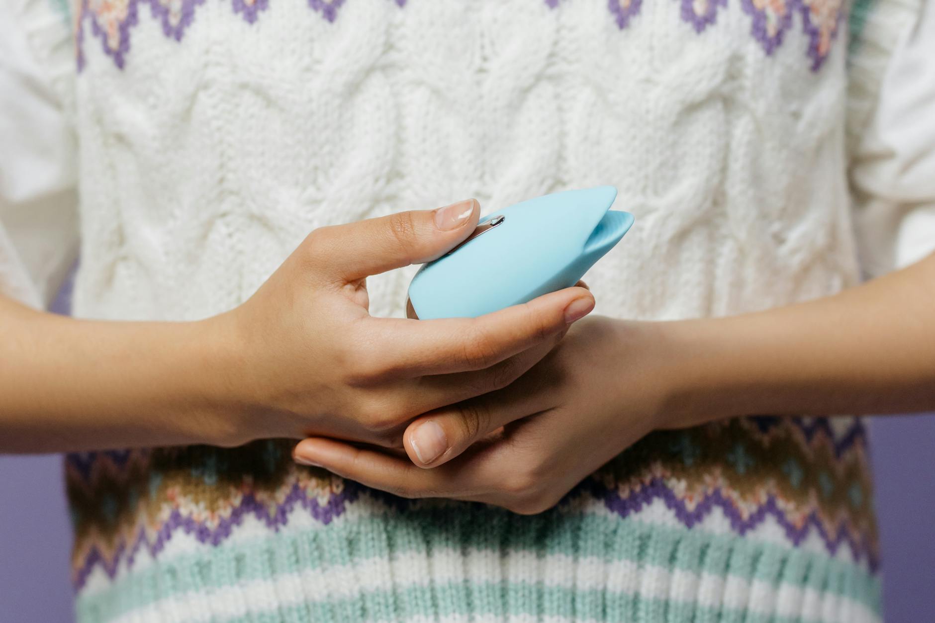 A hand holding a blue silicone lemon vibrator against a soft purple background, demonstrating gentle clitoral stimulation.